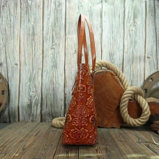 Brown leather handbag with intricate patterns on a wooden surface with a rustic background.