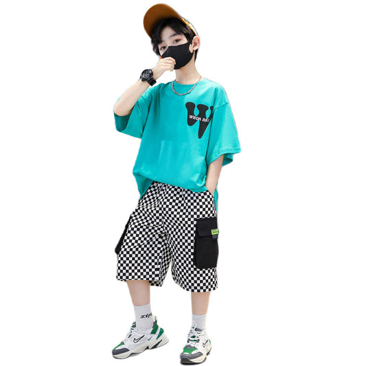 Person wearing a turquoise t-shirt with a logo, checkered shorts, and sneakers on a white background