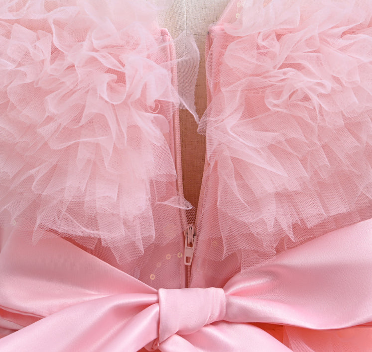Close-up of a pink dress with ruffled sleeves and a large bow detail.