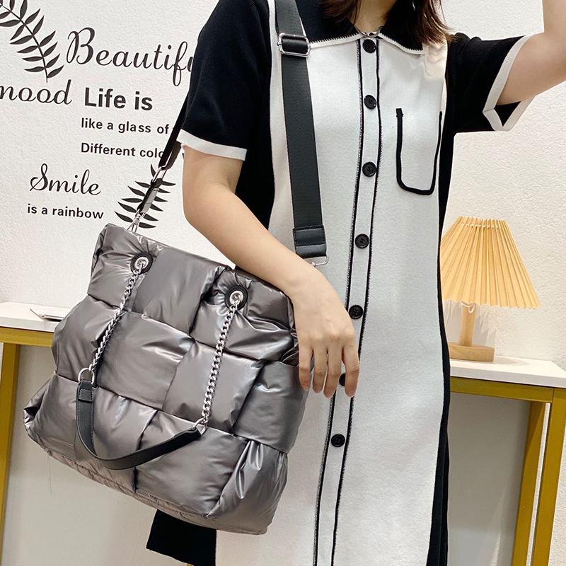 Person holding a silver quilted handbag with a decorative chain in a room setting.