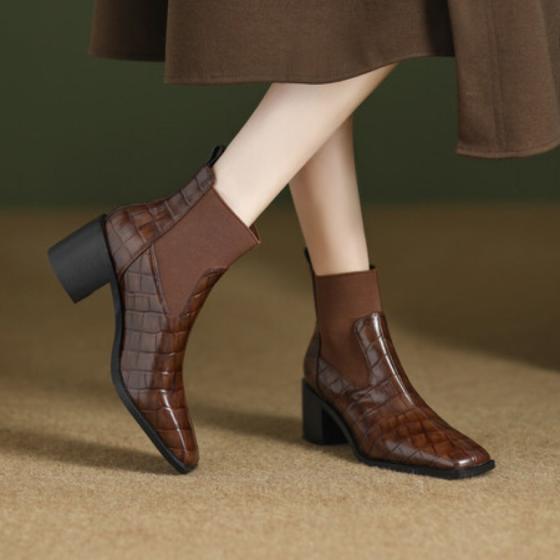 Brown ankle boots with a textured pattern worn by a person on a beige surface.
