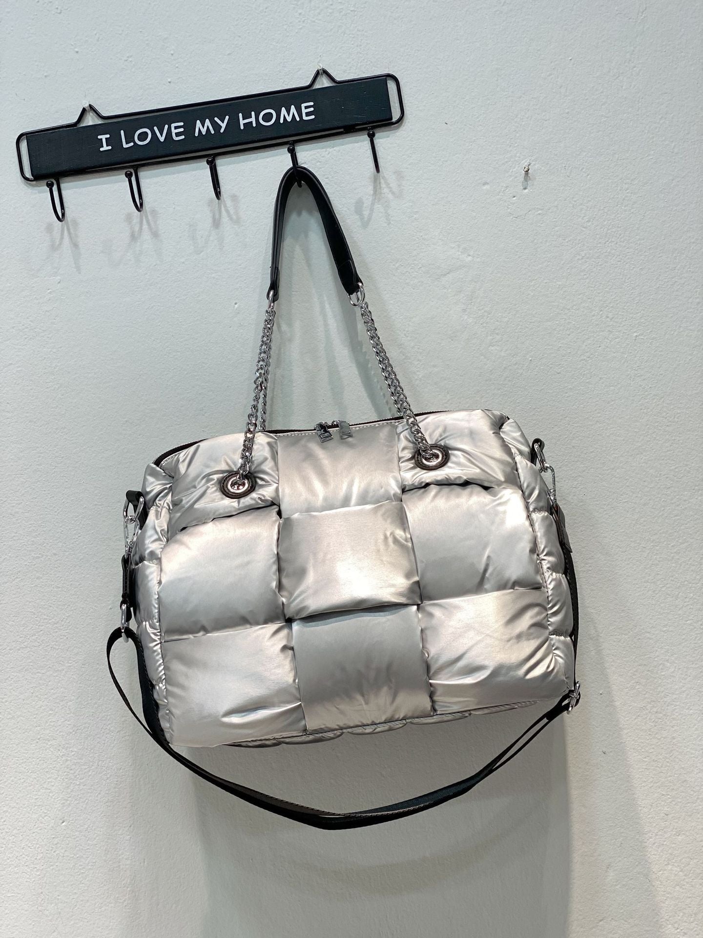 Silver quilted handbag hanging on a wall hook with 'I Love My Home' sign.