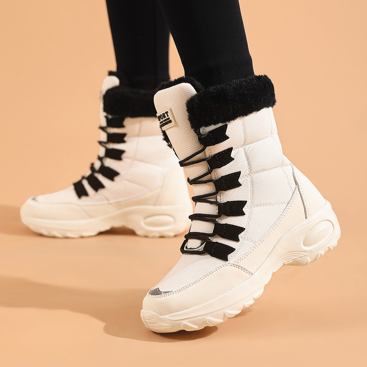 White mid-calf winter boots with black laces and a black faux-fur collar, shown on a model wearing black leggings against a solid peach background.