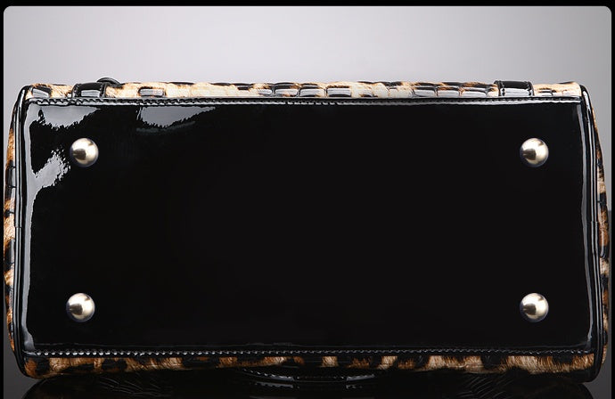 Black patent leather handbag with leopard print trim on a gray background