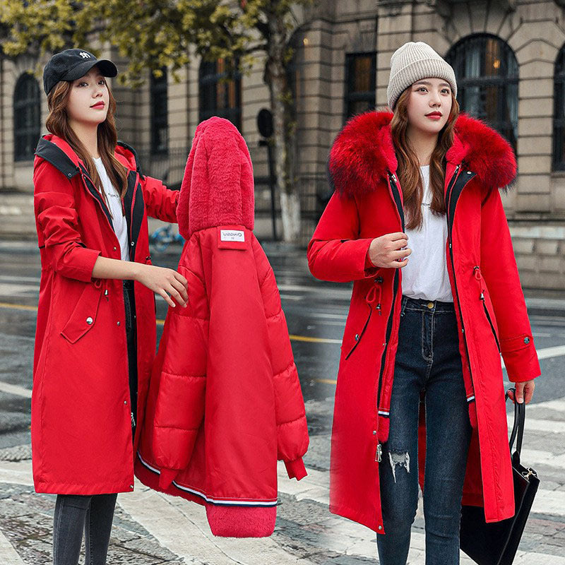 Two women wearing red puffer jackets with fur hoods on a city street.