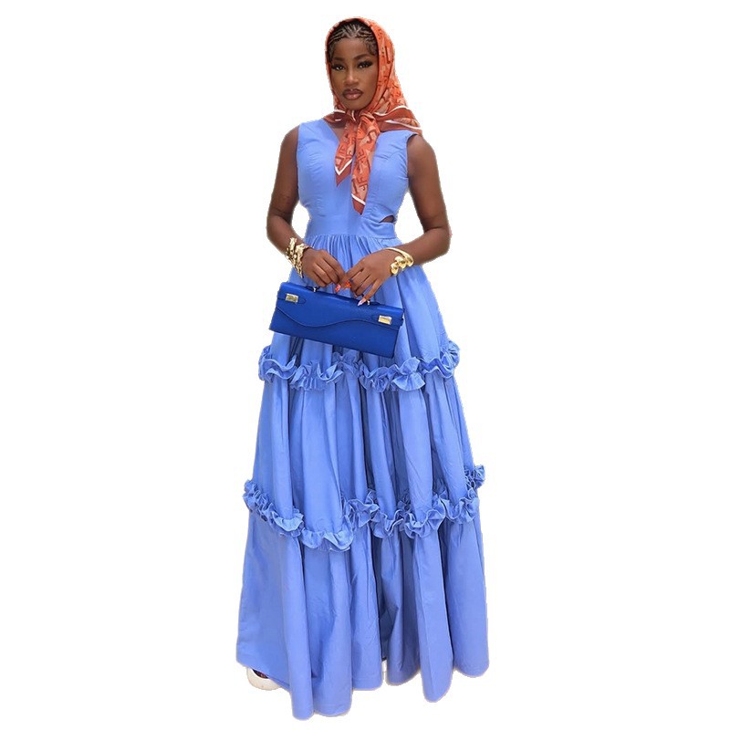Woman wearing a long blue dress with ruffles and an orange headscarf on a white background