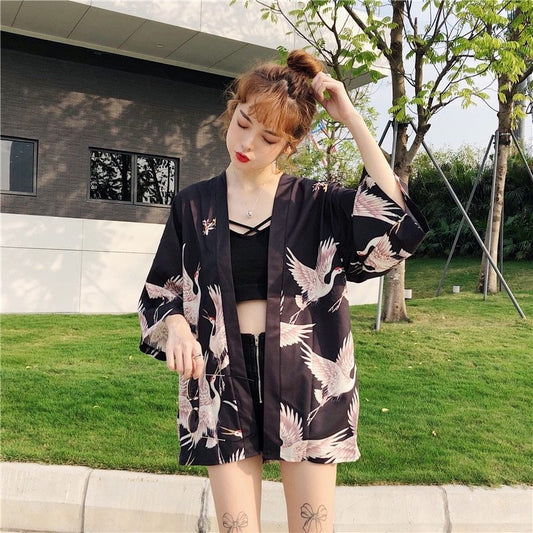 Woman wearing a black kimono with crane patterns outdoors.