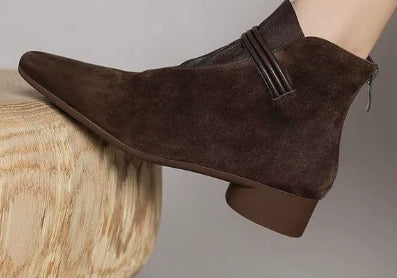 Brown suede ankle boots on a wooden surface with a neutral background