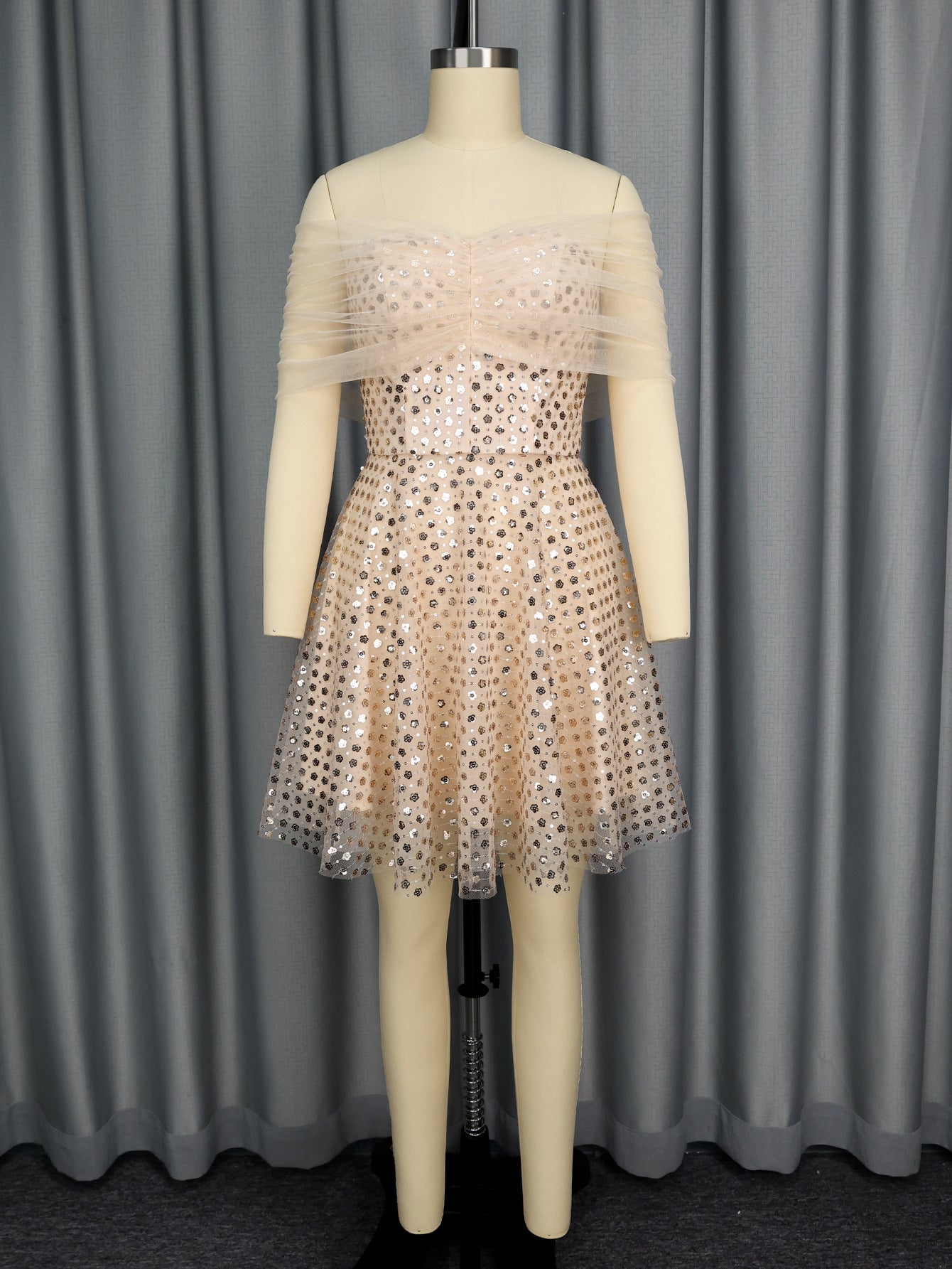 Mannequin wearing a beige dress with sequin details against a gray curtain background