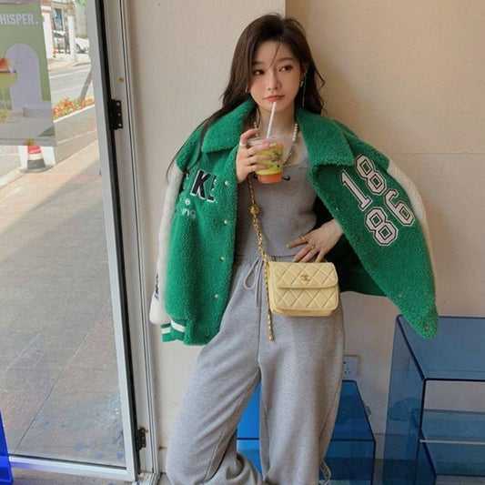 Woman wearing a green jacket with 'K1986' text, holding a drink and a yellow handbag.
