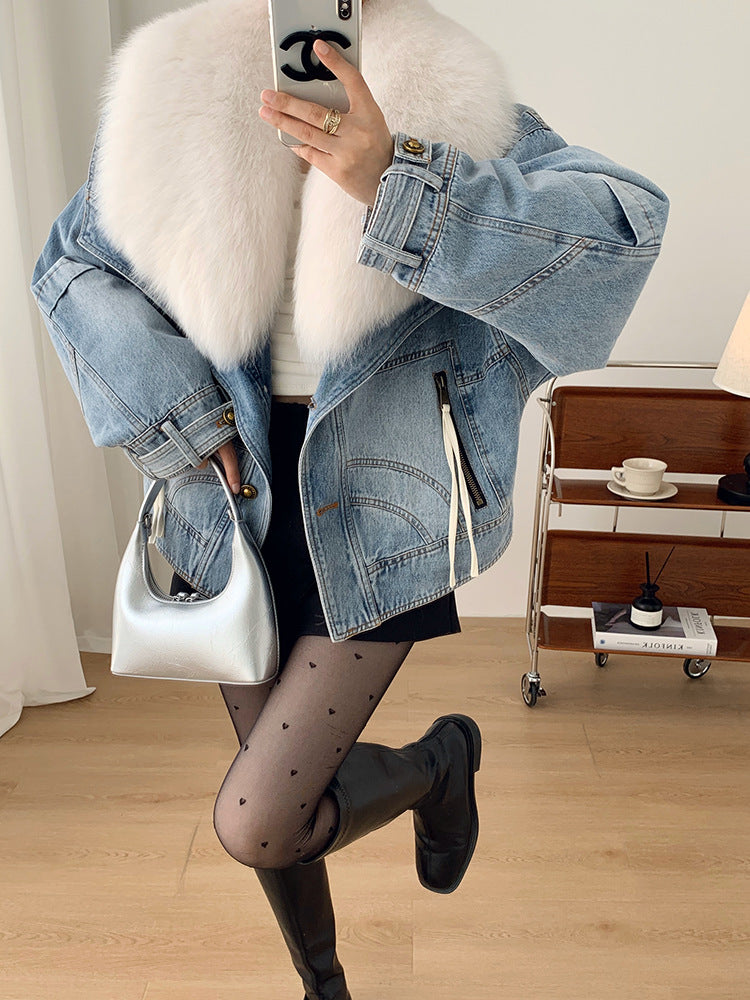 Person wearing a denim jacket with a fur-lined hood, holding a phone, in a room with a wooden floor and a small table.