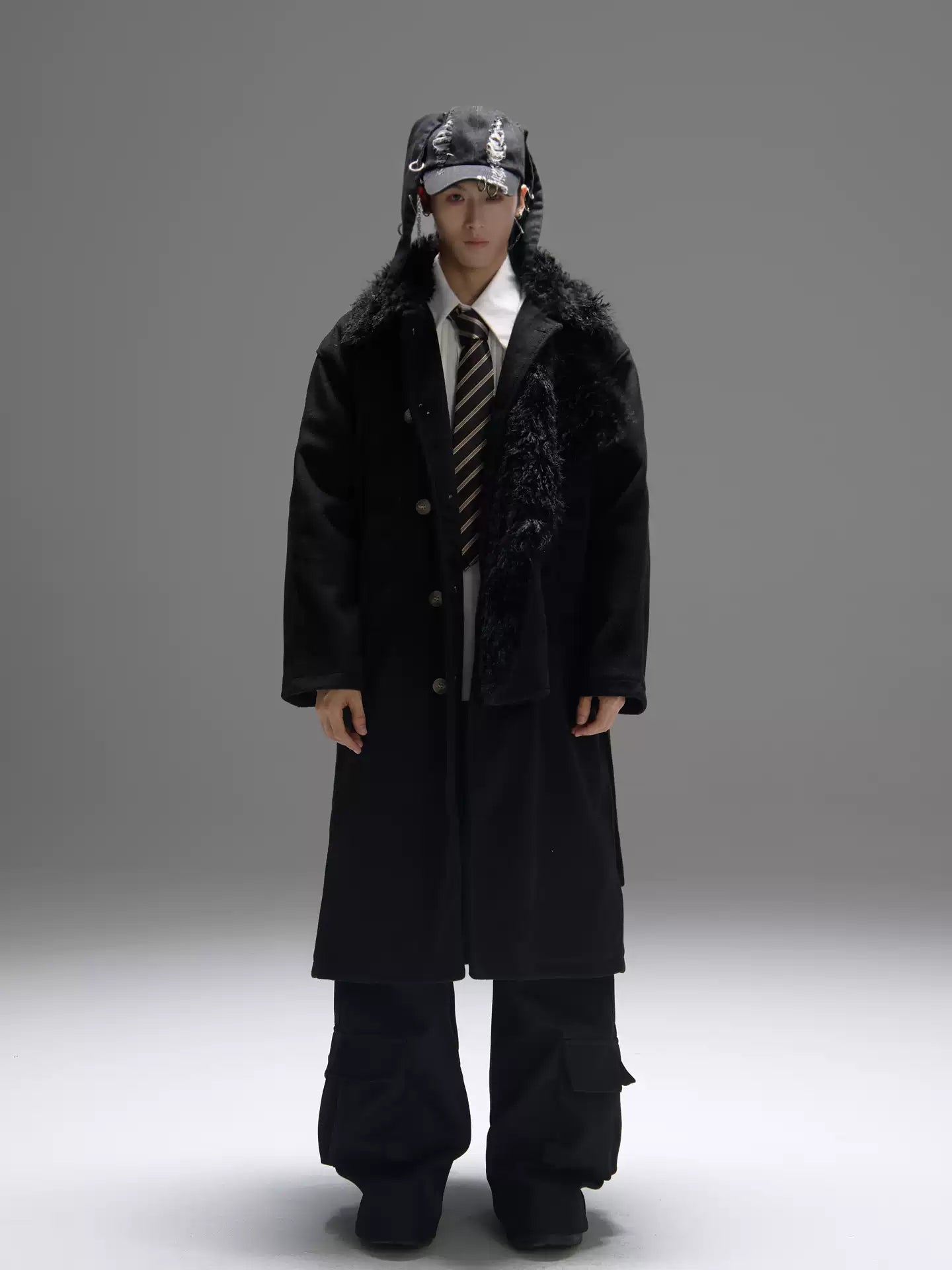 Person wearing a long black coat with fur trim on a gray background