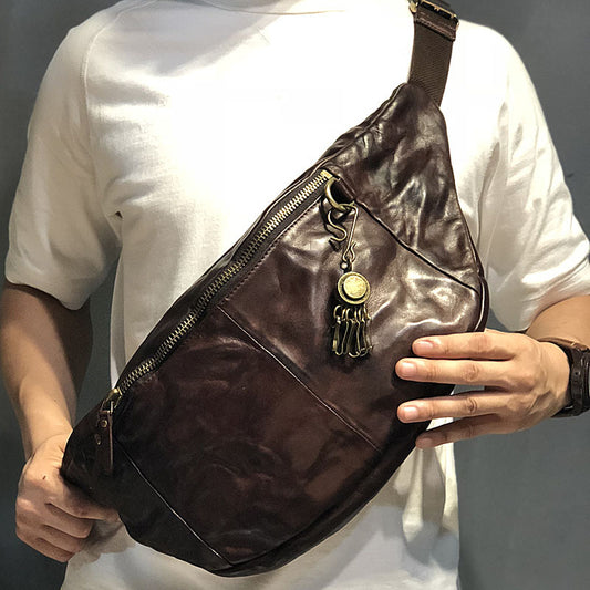 Brown leather bag with decorative charm held by a person wearing a white shirt.