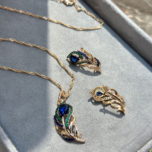 Gold necklace with peacock feather design on a gray surface