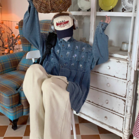 Person wearing a denim jacket and beige pants sitting on a white chair in a room with a plaid couch and decorative items.