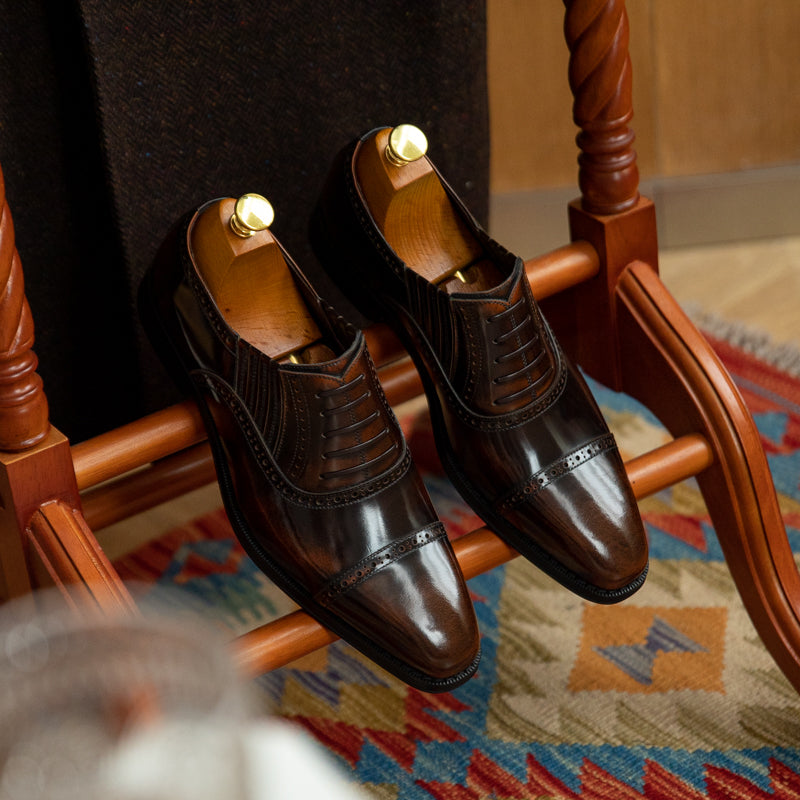 Pair of brown dress shoes on a wooden chair with a patterned rug underneath
