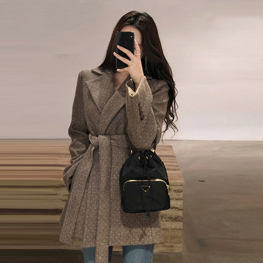 Woman taking a mirror selfie wearing a brown coat and black backpack.
