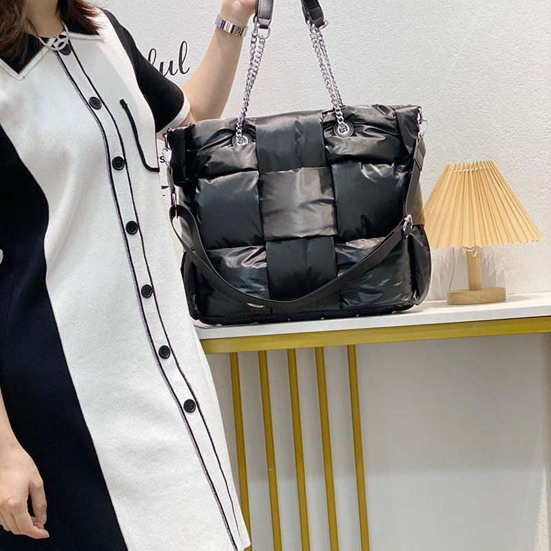 Person holding a black quilted handbag with a chain strap in a minimalistic room.