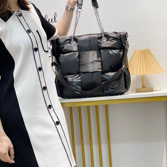 Person holding a black quilted handbag with a chain strap in a minimalistic room.