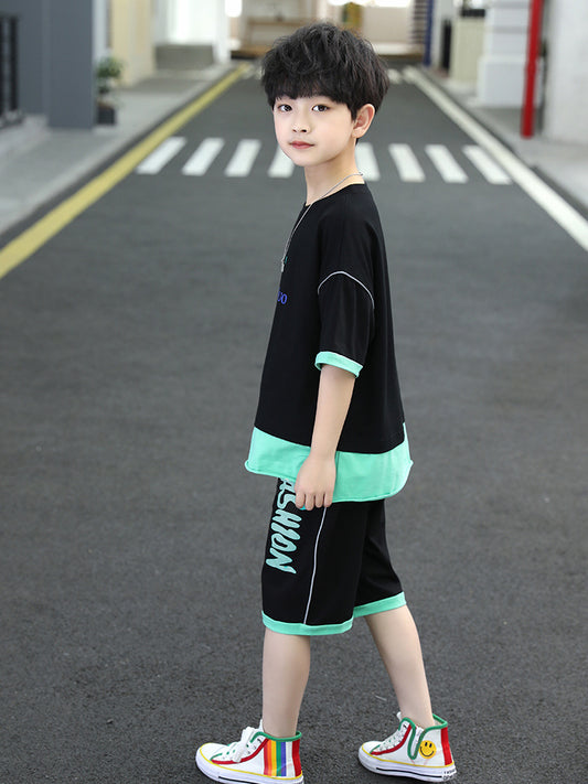 Child wearing a black and green outfit with colorful sneakers on a road.