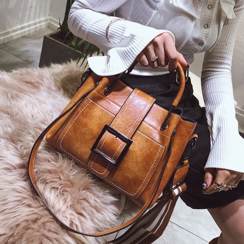 Brown leather handbag with a buckle detail held by a person on a fluffy rug.