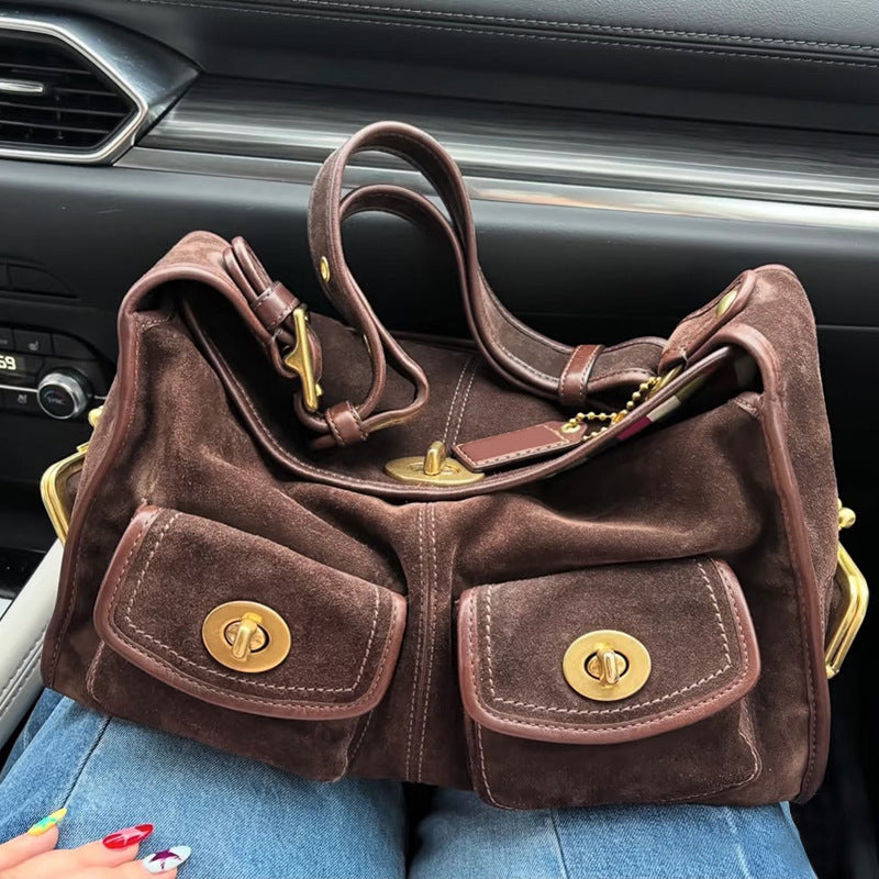 Brown suede handbag with gold accents on a lap inside a car.