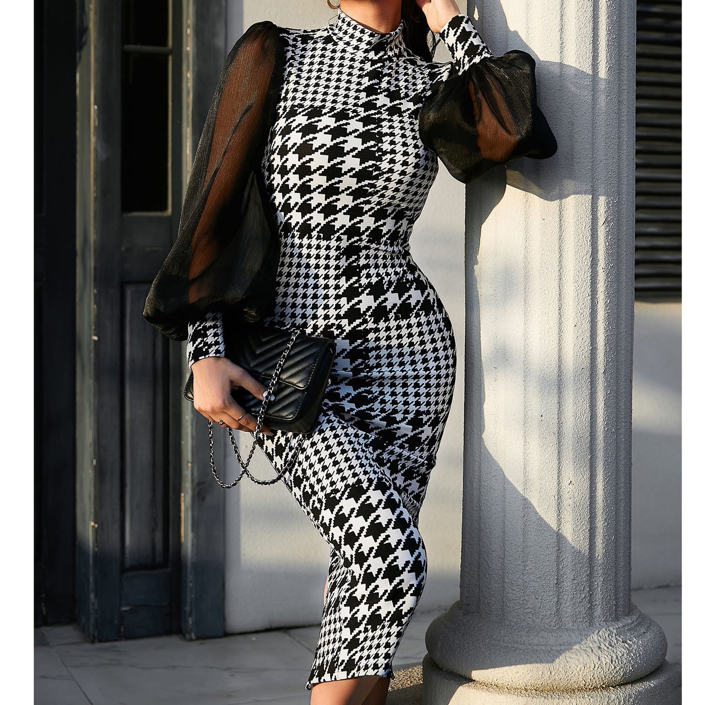 Person wearing a black and white houndstooth pattern outfit holding a black handbag.