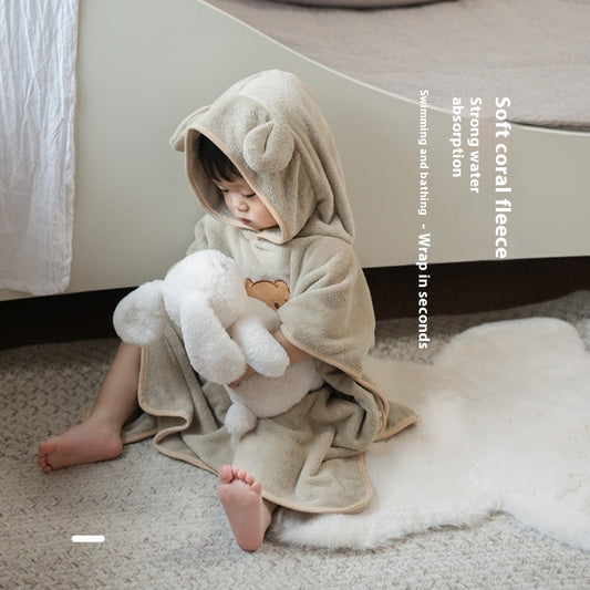 Child wrapped in a soft coral fleece towel with bunny ears, sitting on a carpeted floor.