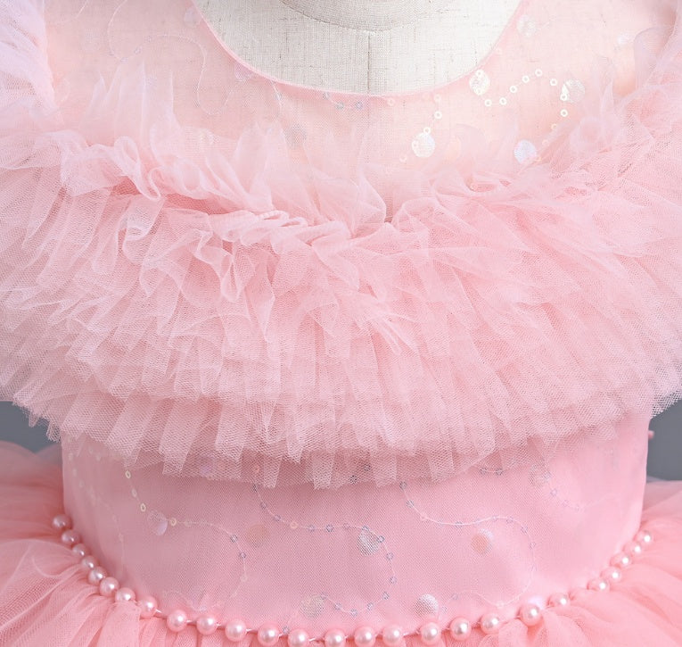 Close-up of a pink tutu dress with ruffles and pearl details on a gray background