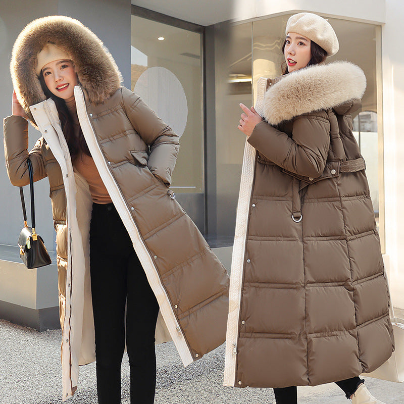 Woman wearing a long brown puffer coat with a fur-lined hood in an urban setting.