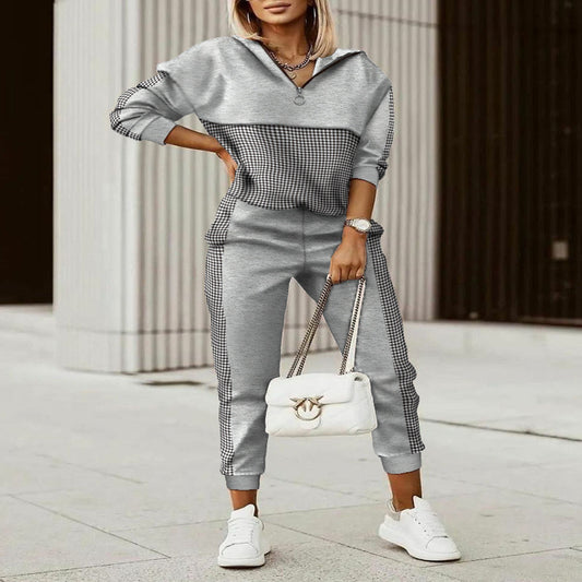 Woman in a stylish outfit with a gray and black checkered top and pants, holding a white handbag.