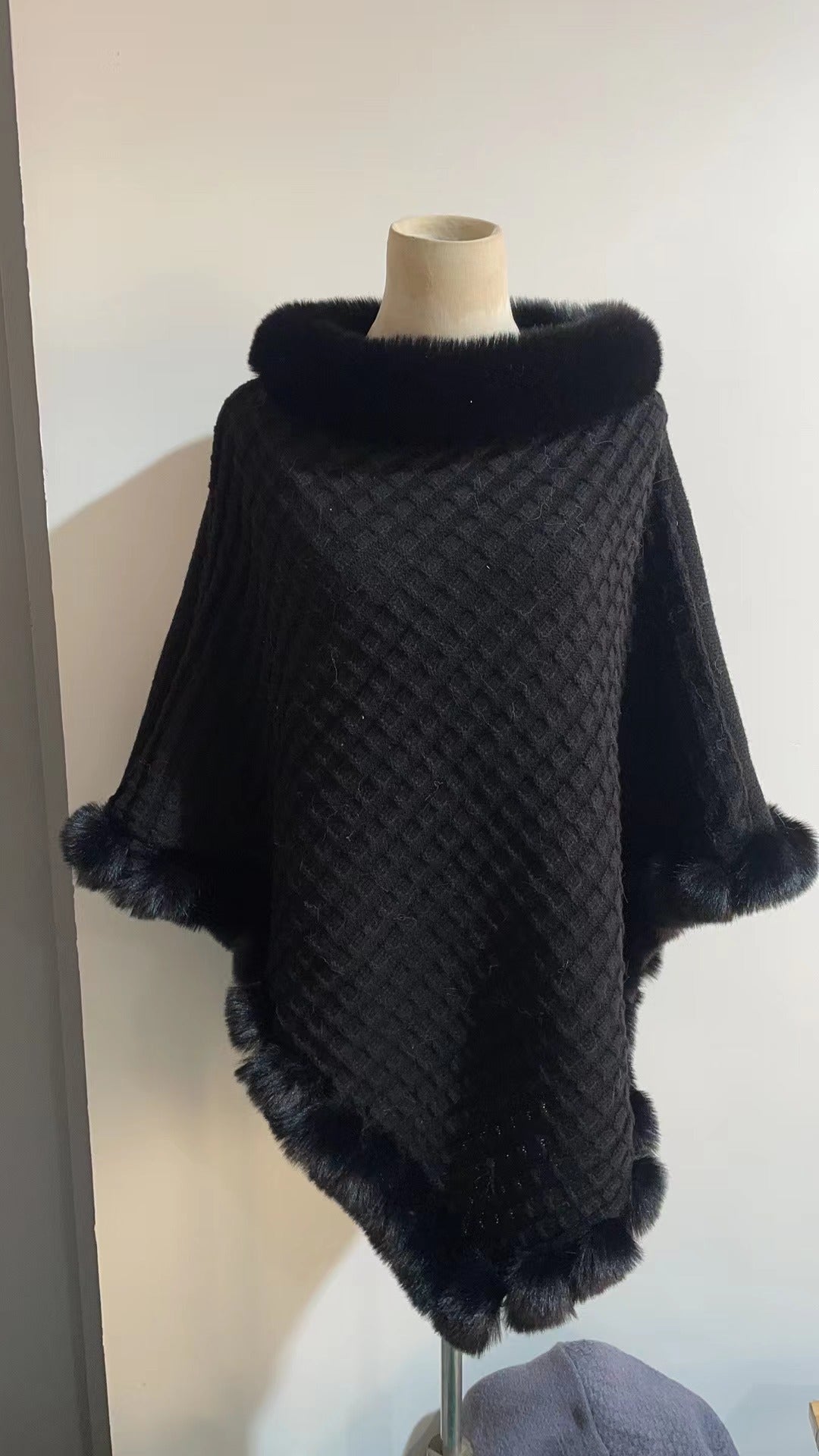 Dark gray quilted poncho with fur trim on a mannequin against a white background