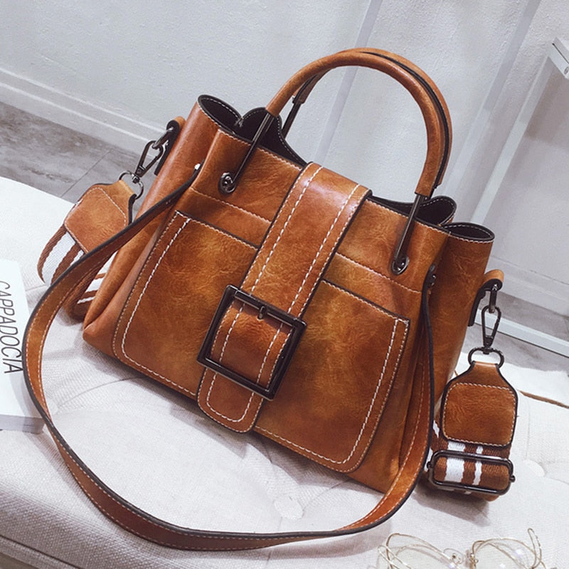 Brown leather handbag with a matching keychain on a light surface.