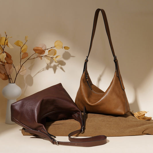 Two brown leather handbags on a beige surface with a vase of flowers in the background.