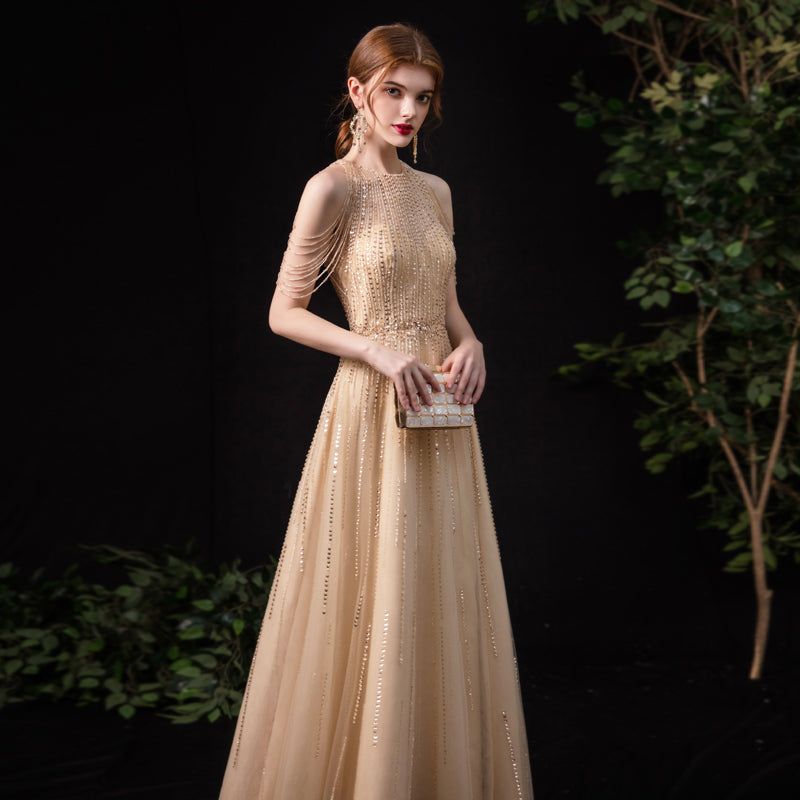 Woman wearing a beige evening gown with intricate detailing against a dark background