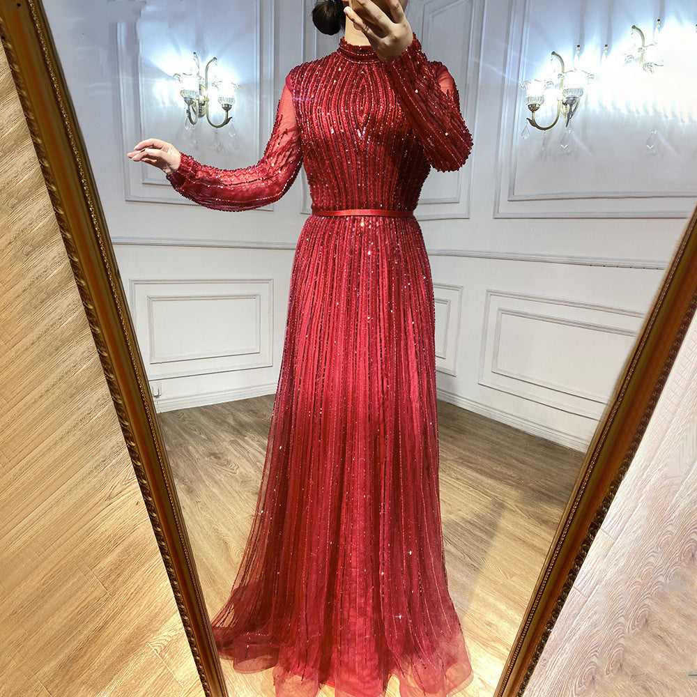 Red evening gown with long sleeves and a fitted bodice, worn indoors.