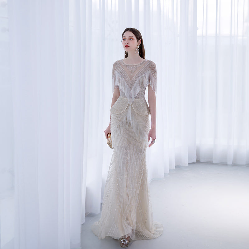Woman wearing a long, elegant dress with intricate detailing in a softly lit room.