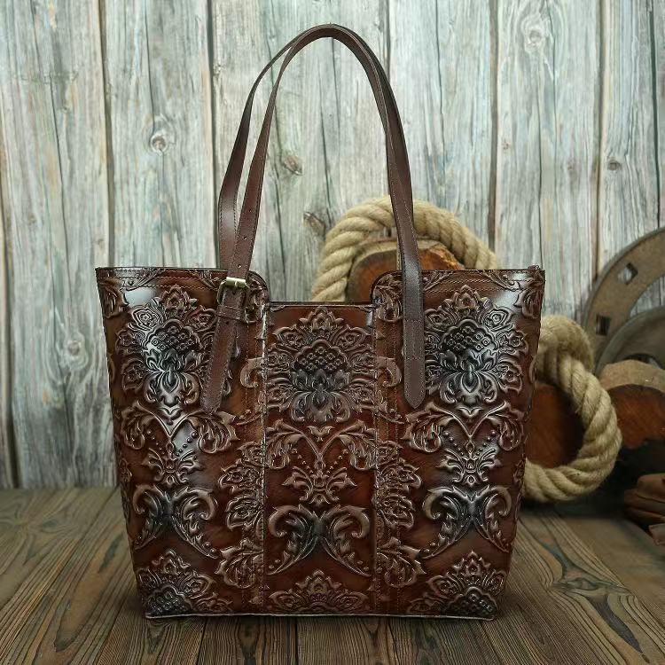Brown leather tote bag with intricate patterns on a wooden surface.