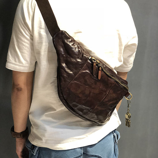 Person wearing a brown leather sling bag with a keychain on a plain background