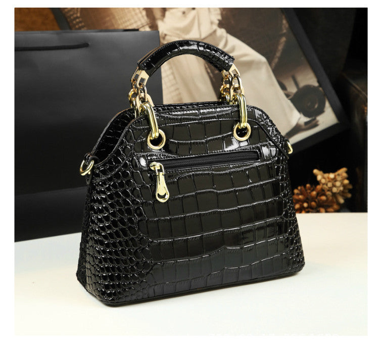 Black crocodile-patterned handbag with gold accents on a white surface.