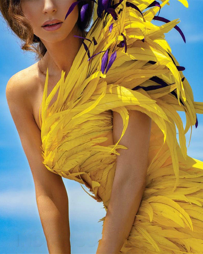 Person wearing a bright yellow feathered dress against a clear blue sky.
