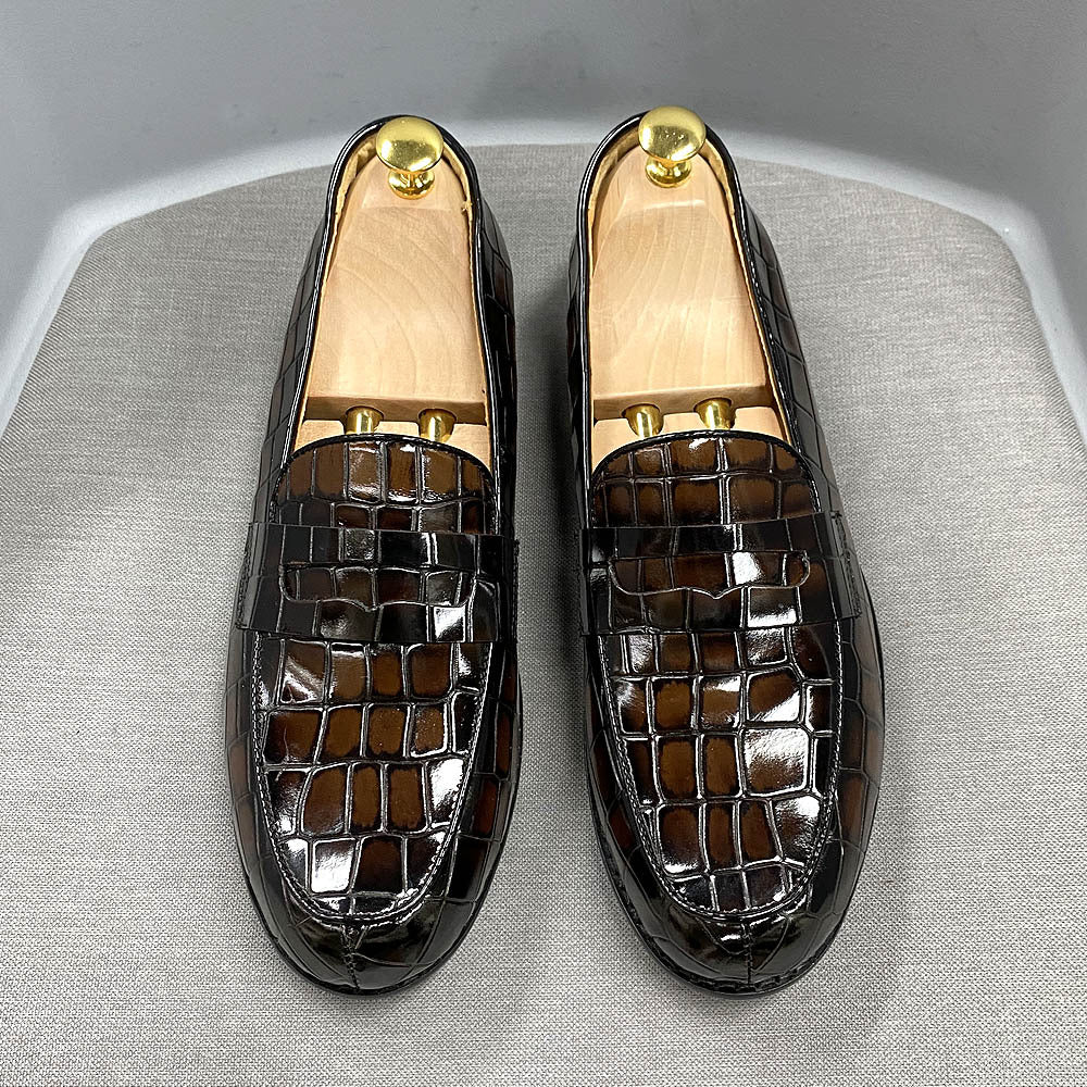 Pair of black crocodile-patterned loafers on a gray surface
