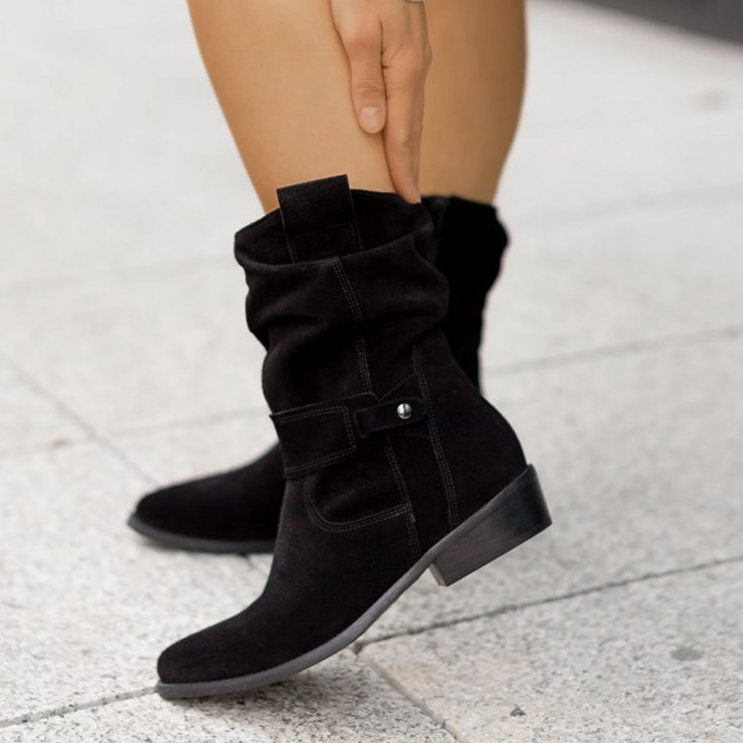 Black suede boots worn by a person on a light gray pavement.