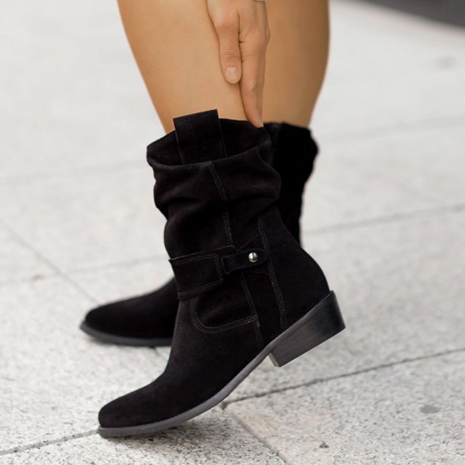 Black suede boots worn by a person on a light gray pavement.