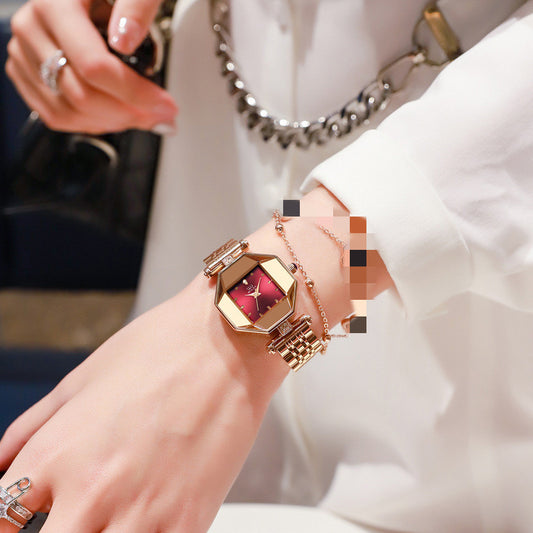 Close-up of a person's wrist wearing a gold watch with a red face.