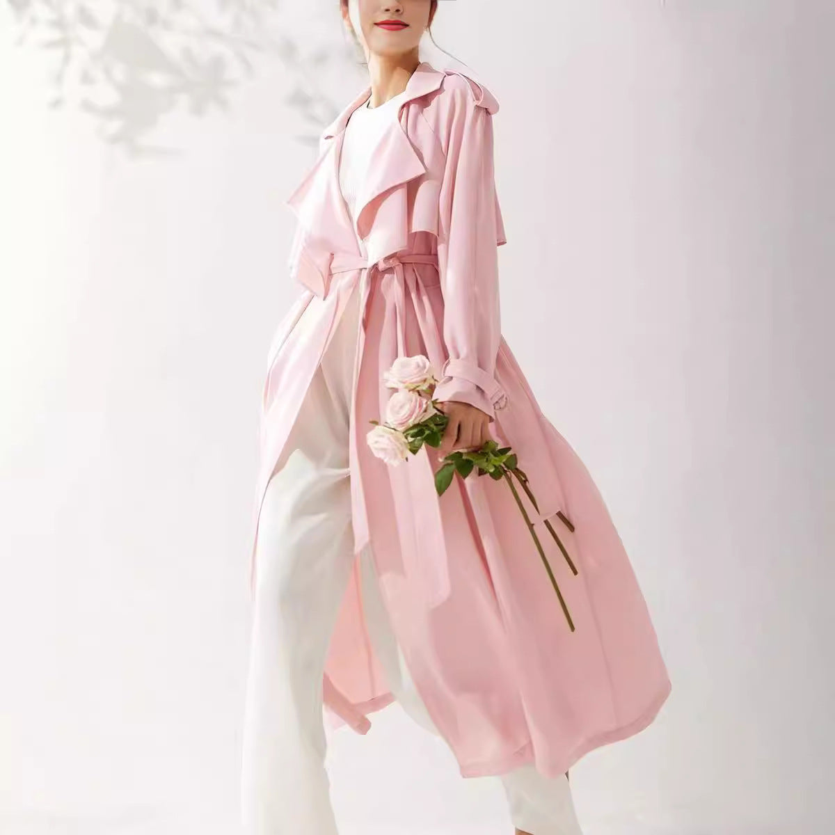 Person wearing a pink trench coat holding flowers against a white background