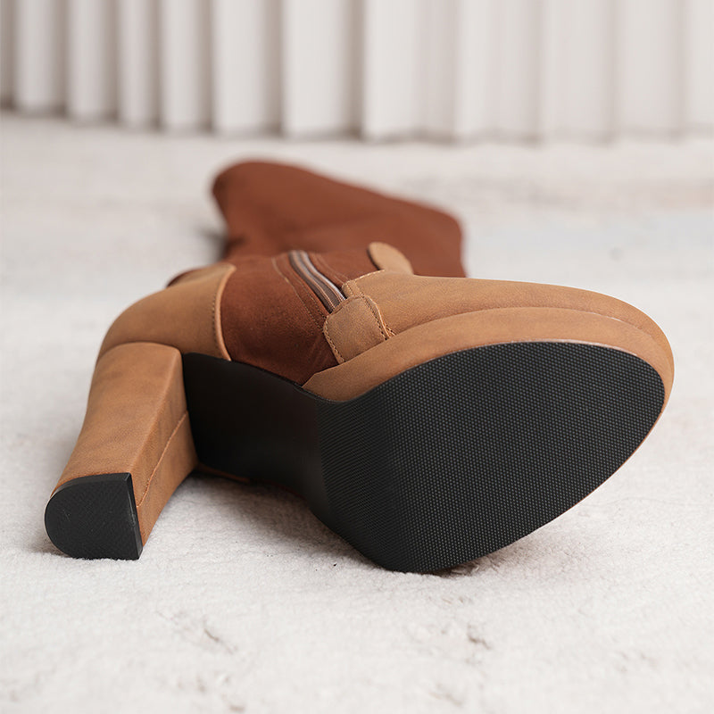 Pair of brown suede boots with black soles on a light background