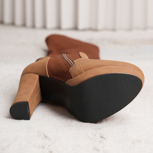 Pair of brown suede boots with black soles on a light background