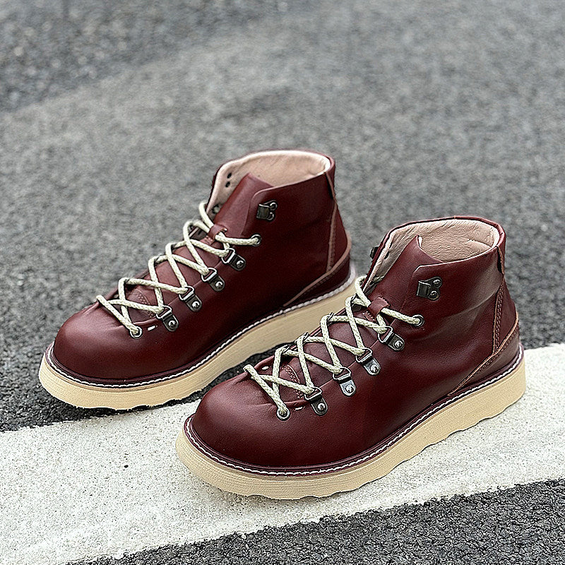 Pair of maroon leather boots with white soles on a gray pavement background