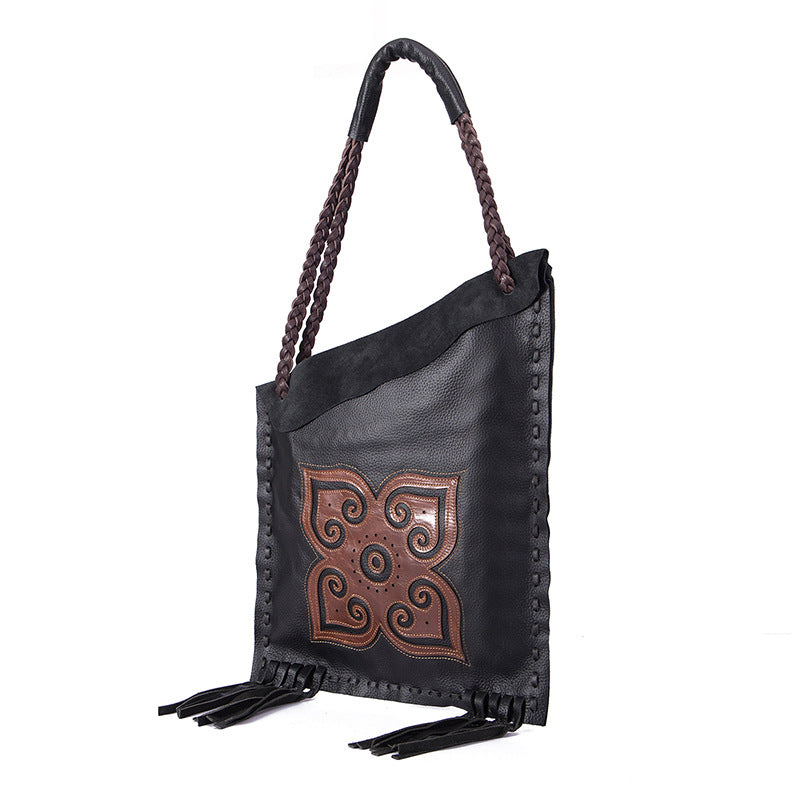 Black leather handbag with brown decorative emblem and tassels on a white background